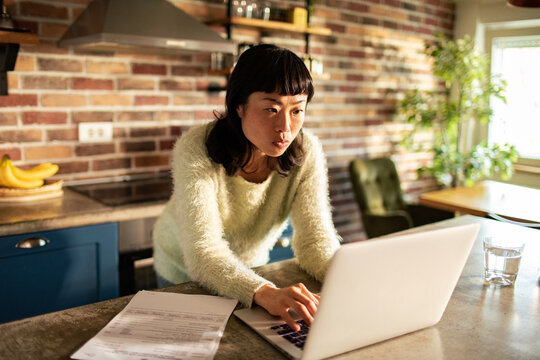 Focused woman paying bills online in home kitchen