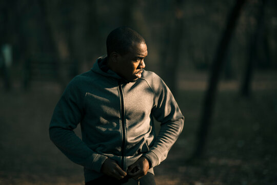 Athletic man zipping hoodie before running in forest park at sunrise