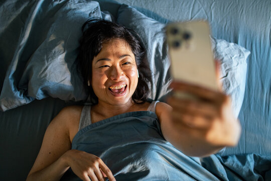 Smiling woman video chatting in bed at home