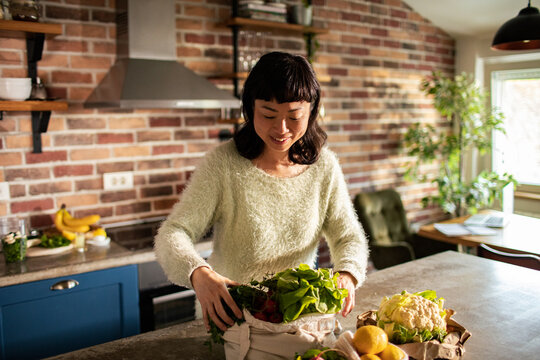 Smiling woman unpacking fresh groceries in home kitchen