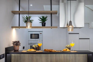 Contemporary breakfast bar with juice, pastries, pendant lights, and modern kitchen background