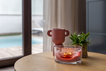 Close-up of cozy decor with candle, plant, and ceramic vase near poolside window table