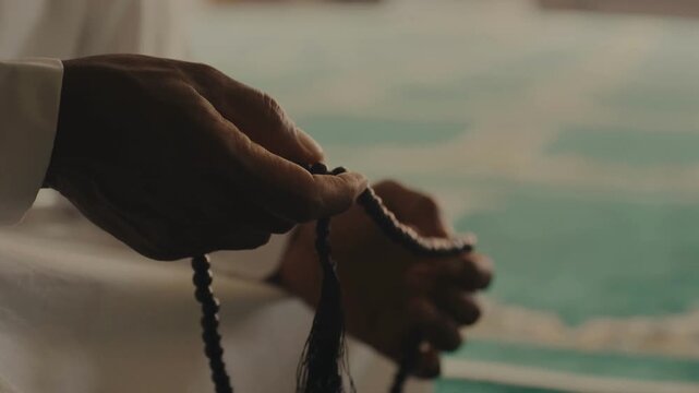 A man&rsquo;s hand holding a prayer beads while praying