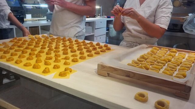 Chefs preparing rows of handmade tortellini pasta in a commercial kitchen setting. Bologna tortellini hands made