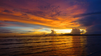 Serene orange lit sunset shining on tranquil ocean, beaches and lonely boats.