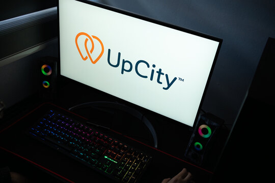 Punta Arenas, Chile &ndash; January 20, 2026: A desktop monitor featuring the stylized UpCity wordmark and "adjoining pins" symbol alongside glowing peripherals