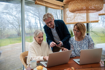 Three mature adults collaborating on laptops in a bright home conservatory