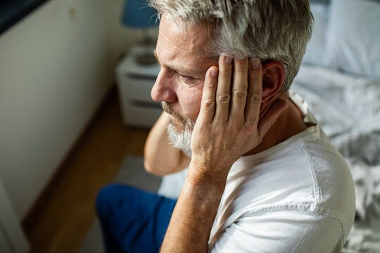 Middle-aged man covering ears in bedroom at home