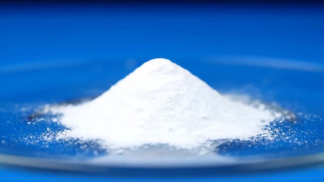 White Titanium Dioxide Powder on Glass - A mound of fine white titanium dioxide powder sits on a clear glass plate against a vibrant blue background. The powder forms a small hill, catching the light.