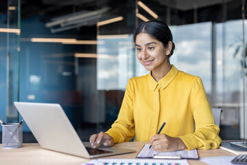 Young Indian businesswoman working in an office at a desk with a laptop and signing documents