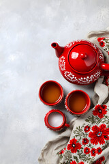 Red teapot and cups arranged on a light background with a decorative cloth featuring flowers and patterns