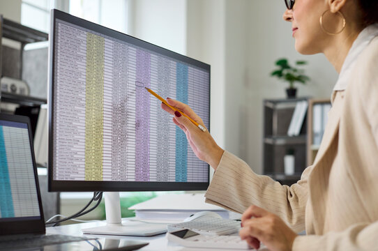 Accountant conducts audit and finance analysis. Business analyst reviews spreadsheet data on a computer monitor, checking report accuracy in an office. Concept shows precise financial oversight.