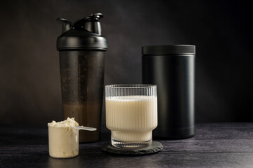 Protein drink in a glass with protein shaker and tube on dark background. Body building, muscle growth and food supplement concept