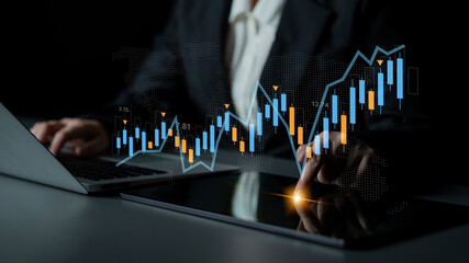 A business professional uses a laptop and tablet to analyze financial market data, showcasing stock trends and graphs in a dark workspace. Perfect for finance themes. Gantry