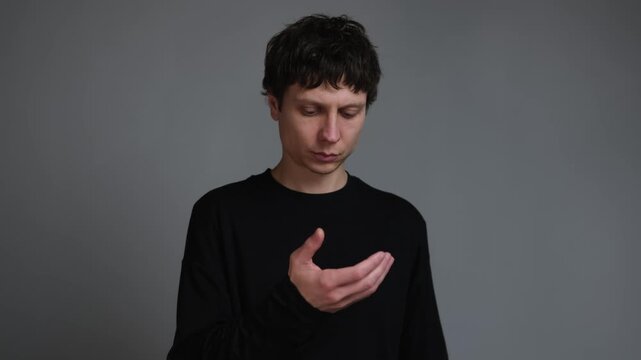 Attention disorder and restless focus in phantom phone reach. young man looking at empty hand on neutral grey background.