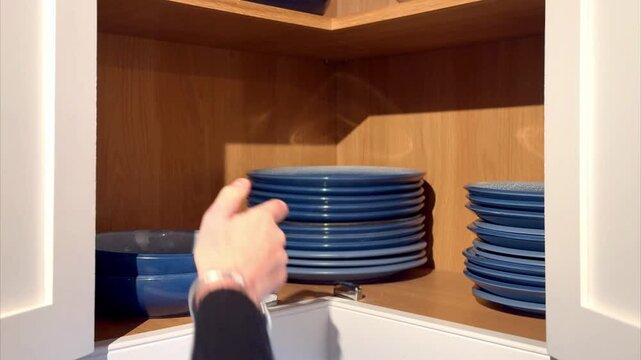 woman placing blue bowls in crockery cupboard with stacked plates in kitchen