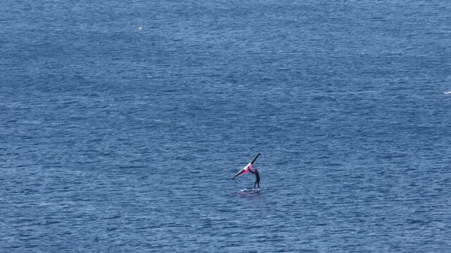 Hydrofoil windsurfer with pink foil rides waves on the open Adriatic Sea. Real time high-angle view of extreme sport in the Kvarner Bay, Croatia. Sporty lifestyle, windy day active vacation.