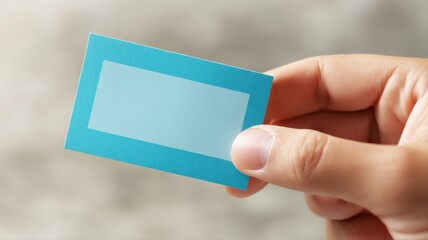 Obraz premium Hand Holding Blank Blue Card for Mockup, Message, or Presentation Against a Neutral Background
