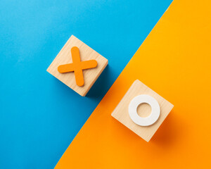 Minimalist wooden blocks with orange X and white O symbols on a split blue and orange background. Conceptual image for tic-tac-toe, strategy, decision-making, competition, and business choice.
