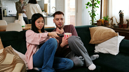 Obraz premium Couple enjoying a movie night at home, switching channels while eating popcorn