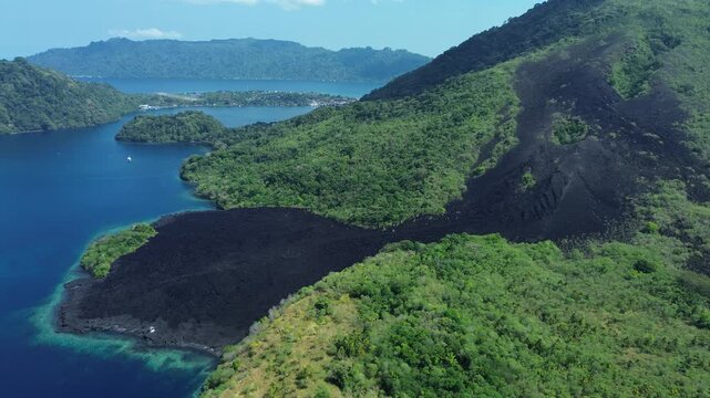 Aerial motion flying toward volcanic coast and tilting down to black lava field, Banda Sea, Maluku, Indonesia.