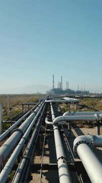 Converging pipelines extending toward refinery complex in arid landscape. Static wide shot from pipeline infrastructure perspective.