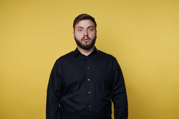 Fototapeta premium Man in black shirt with surprised expression on yellow background.
