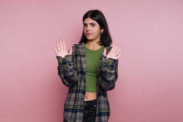 Young woman with hands raised in a stop gesture against pink background.