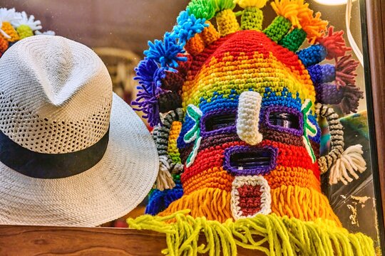 Colorful Aya Uma headdress displayed alongside a traditional straw hat in a souvenir shop, showcasing vibrant patterns and intricate craftsmanship with copy space