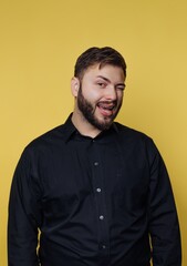 Fototapeta premium A man with a beard wearing a black shirt, winking playfully against a yellow background