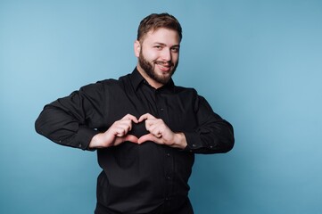 Fototapeta premium Man in black shirt making heart shape with hands on blue background