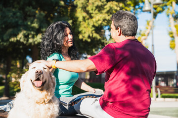 Couple petting happy golden retriever dog in park