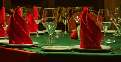 Served table. Green tablecloth, red napkin, wine glasses, white plates. Restaurant service interior...