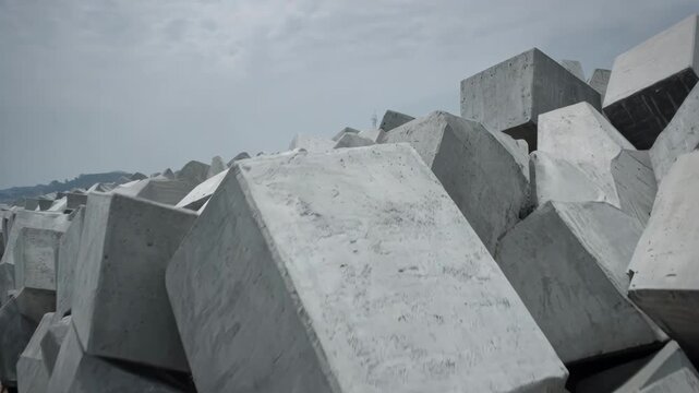 Construction of massive concrete blocks interlocked to form a sturdy marina barrier against ocean waves filmed at medium distance