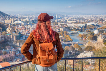 Woman with backpack admiring the panoramic cityscape of Tbilisi, Georgia, from a high viewpoint, experiencing travel and tourism © EdNurg