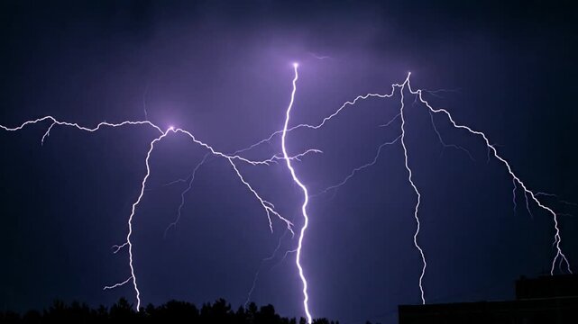 A dramatic lightning storm illuminates the dark sky with multiple bright flashes over a silhouette of buildings and trees at dusk from a distant viewpoint capturing the 0121 event