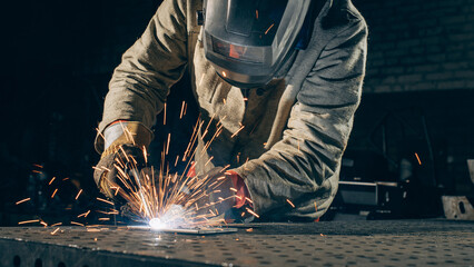 A professional metal worker welds steel in an industrial workshop, wearing protective gear as bright sparks fly from the welding process.