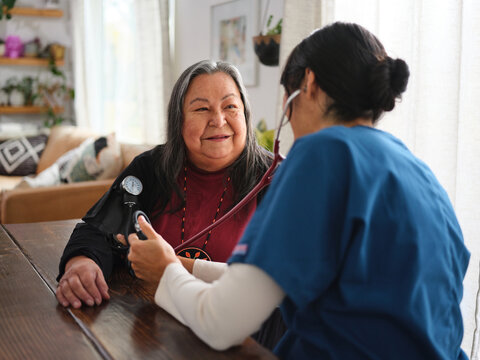 Native American elder patient and nurse sit at table with blood pressure cuff