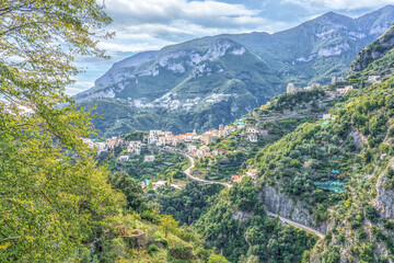 Fototapeta premium Amalfi Coast, Italy. Scenic view of a hillside village nestled among lush green mountains with winding roads and a cloudy sky in the background during daylight hours