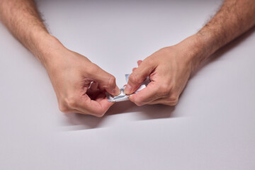Hands extracting capsule from blister pack gently, closeup on fingertips and foil on white tabletop, quiet moment of dosing accuracy and calm preparation for intake