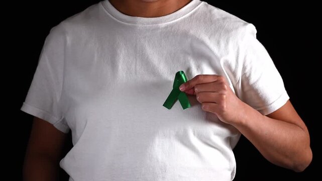 Anonymous woman holding a green ribbon in her hand and bringing it to her chest. Liver cancer awareness and organ donation - Powered by Adobe