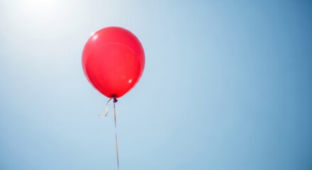 A vibrant red helium balloon floating serenely against a clear blue sky on a bright day