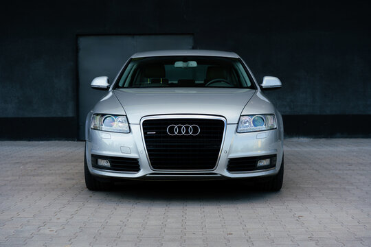 A silver Audi A6 C6 Lift Quattro S Line parked facing forward against a dark building. German design with silver alloy wheels on an empty road. For marketing, advertising, or press releases.