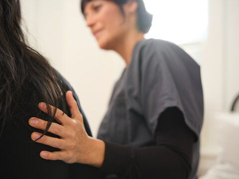 Native American nurse comforts patient with hand on her back in bedroom