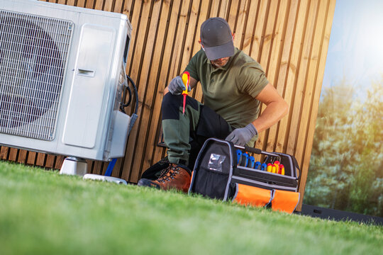 Worker Repairs Air Conditioning Unit in Outdoor Setting