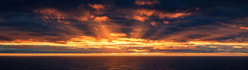 Fototapeta premium Sunrise over ocean horizon with dramatic clouds and warm glowing light reflecting on calm water surface