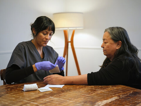 Native American nurse helps elder woman change her bandage at home