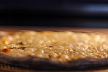 Close up side view of pizza crust baking in oven. Melting cheese and bubbling dough texture.
