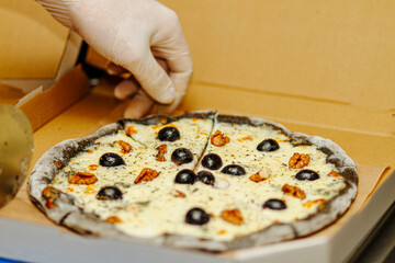 Chef hand arranging walnuts on sliced black cheese pizza in delivery box. Final touch before serving.