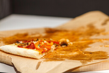 Single leftover slice of meat pizza on greasy parchment paper on wooden board. Last piece of dinner.